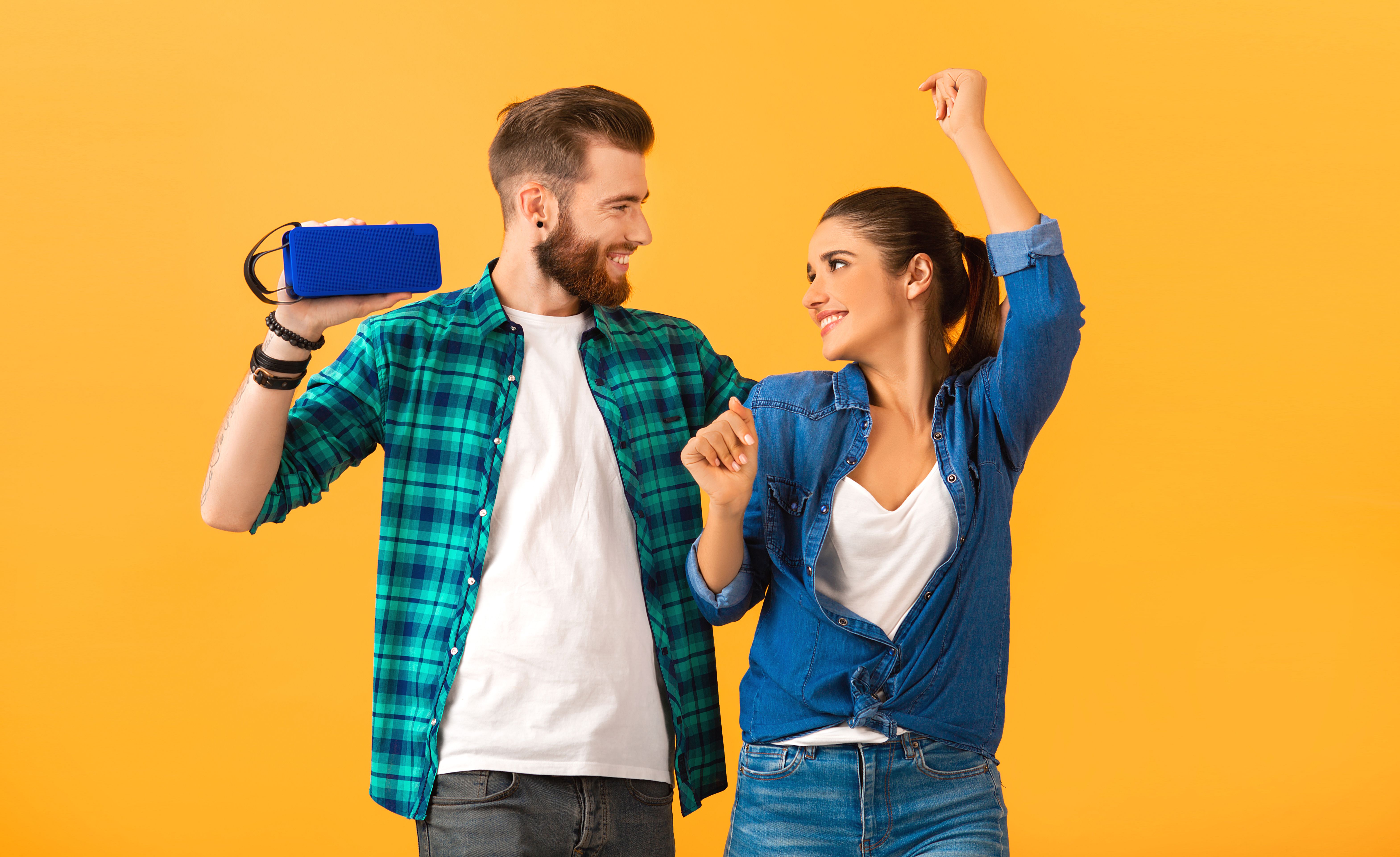 casual-young-couple-holding-wireless-speaker-listening-music-dancing-orange.jpg