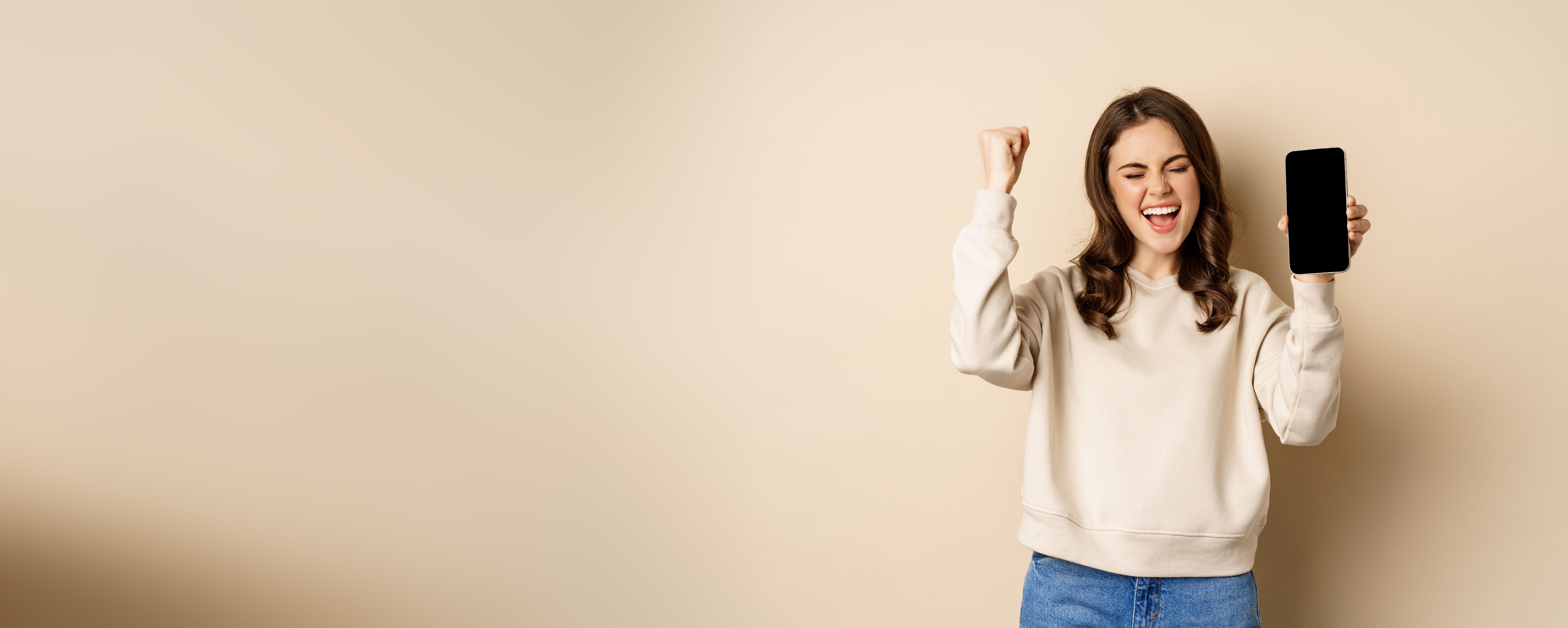 happy-woman-winning-showing-smartphone-screen-shouting-joy-fist-pump-standing-beige-background.jpg