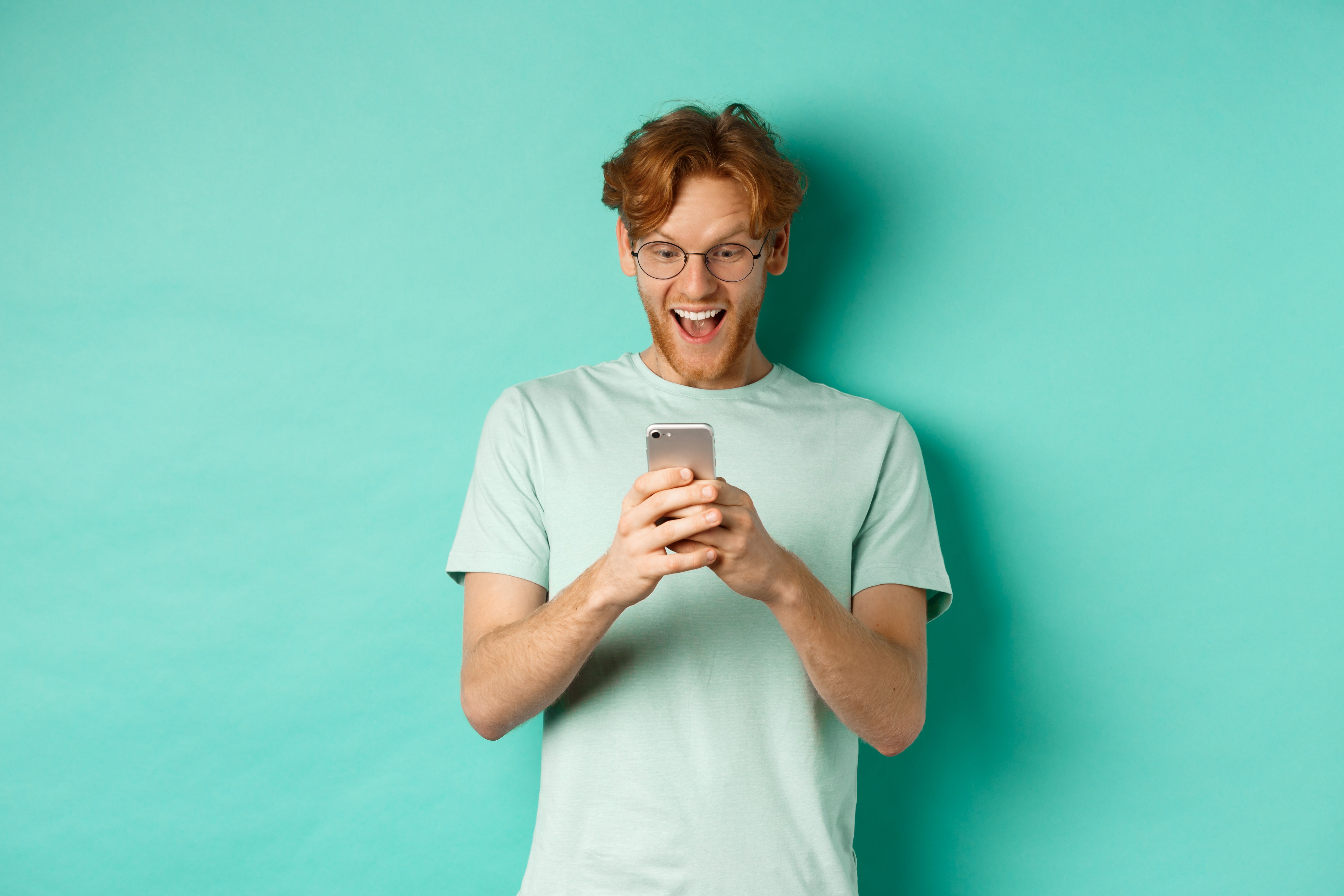 image-young-redhead-man-glasses-reading-phone-screen-with-surprised-face-receive-amazing-promo-offer-standing-turquoise-background.jpg