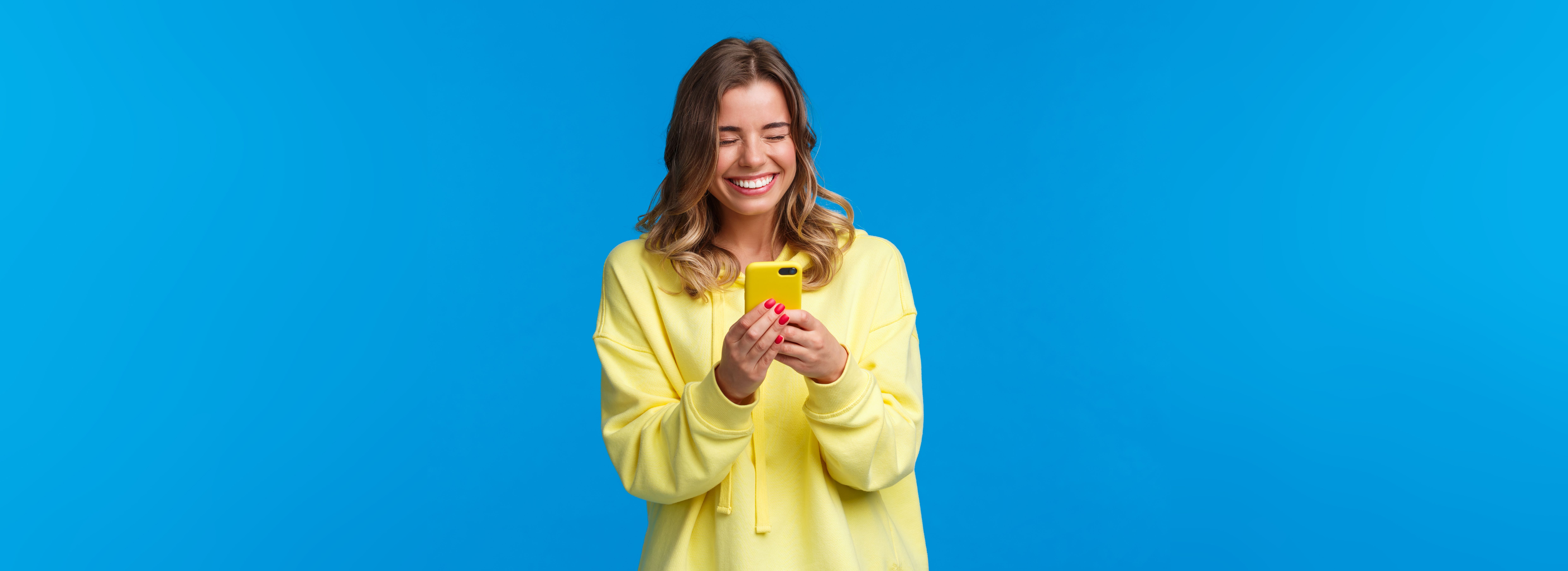joyful-caucasian-female-with-beautiful-smile-yellow-hoodie-holding-mobile-phone-laughing-as-t.jpg