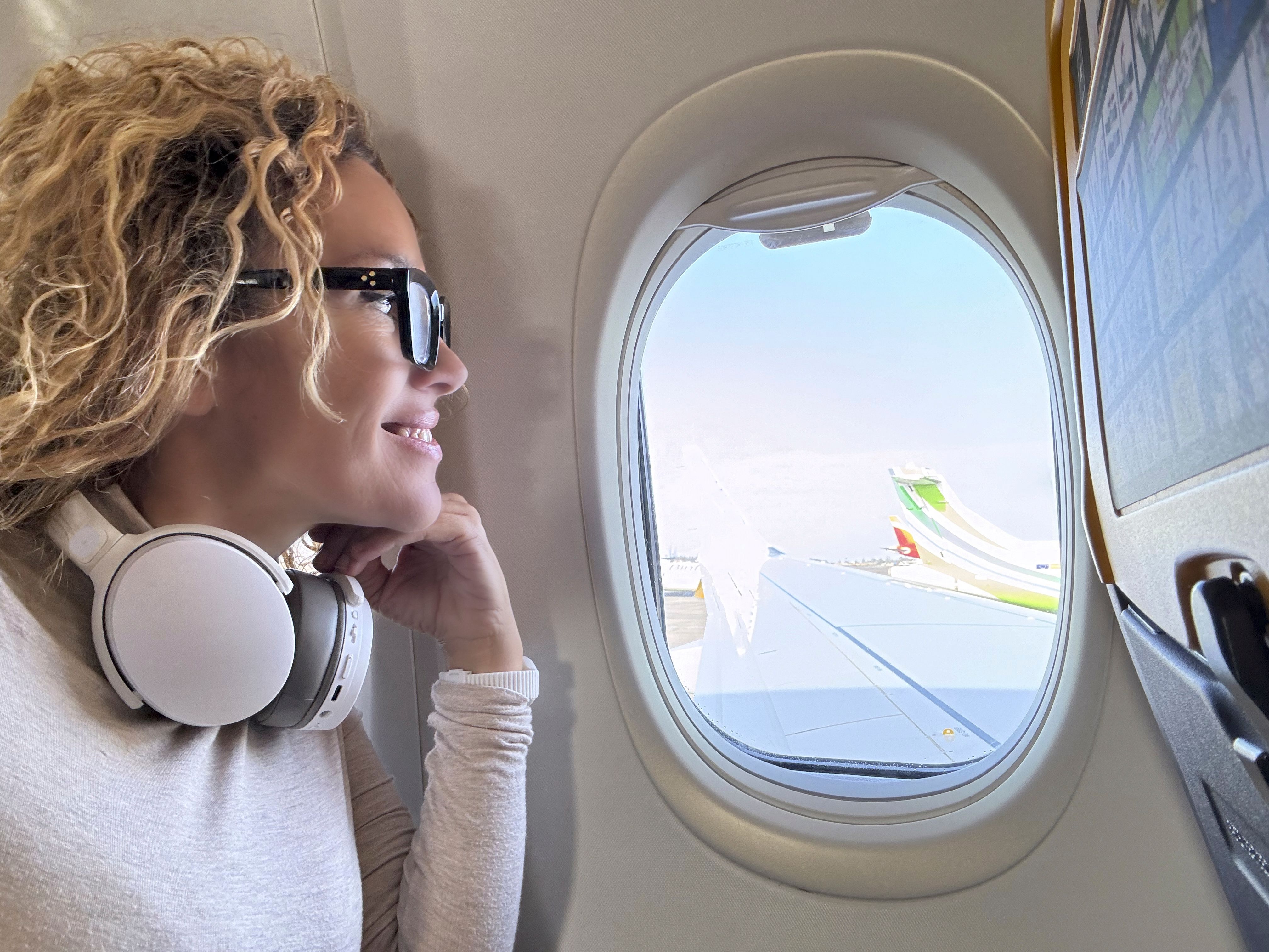 side-view-female-passenger-inside-airplane-flight-looking-outside-window-wing-blue-sky-smiling-enjoying-trip-listening-music-headphones-travel-holiday-vacation-people-happy.jpg