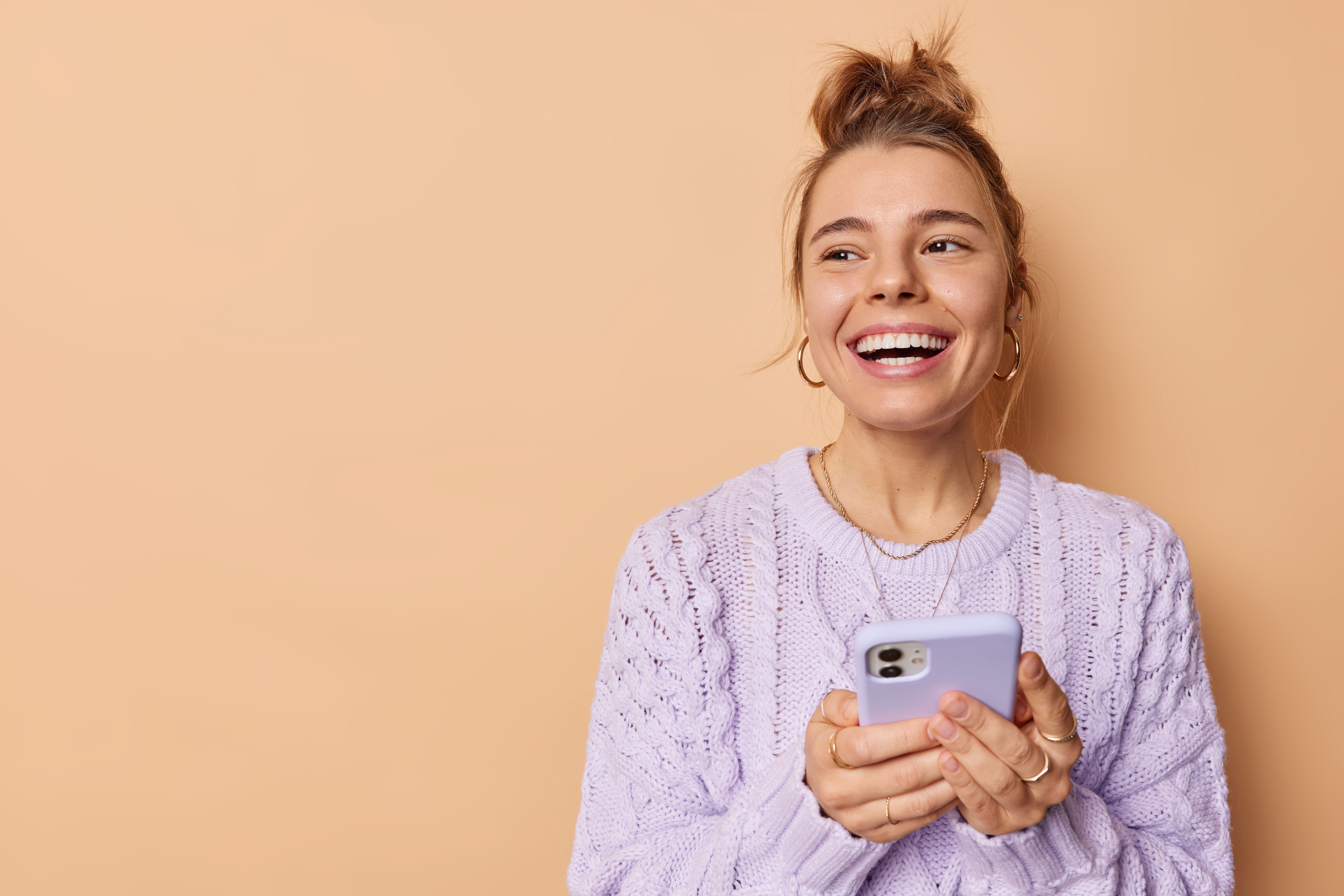smiling-positive-european-woman-with-combed-hair-uses-cellphone-enjoys-modern-technologies-holds-mobile-phone-has-chat-online-wears-casual-sweater-isolated-beige-background-blank-space.jpg