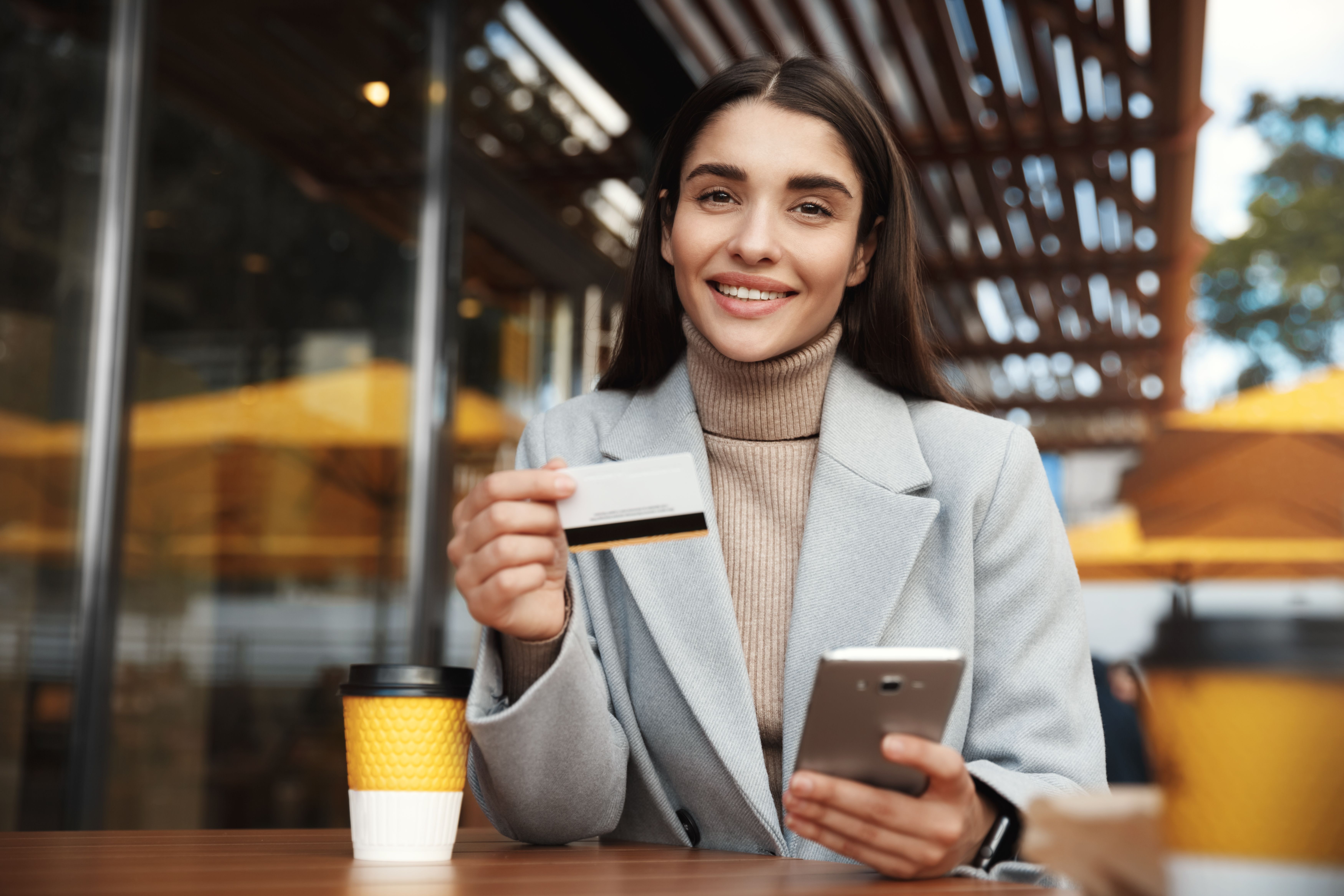 young-woman-paying-online-using-credit-card-mobile-phone-while-sitting-coffee-shop.jpg